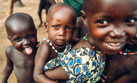 TOPOSA TRIBE, SOUTH SUDAN - MARCH 12, 2020: Girl smiling and carrying baby sibling on back while playing with friends in village on Toposa Tribe in South Sudan, Africaのeditorial素材
