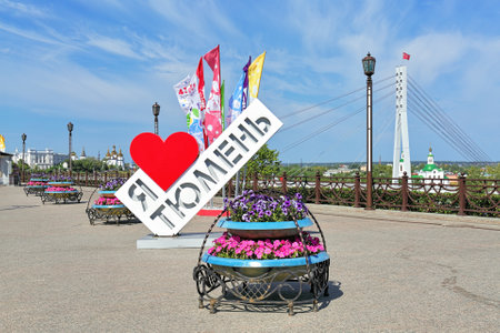TYUMEN, RUSSIA - AUGUST 22, 2016: Art object "I love Tyumen" and flags commemorating the 430th anniversary of the city on the embankment of Tura river near the cable-stayed pedestrian Bridge of Lovers on the background of the city's churches.のeditorial素材
