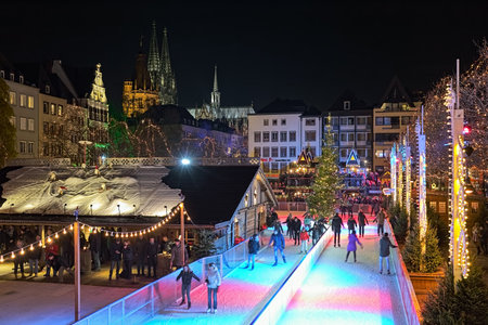 Cologne, Germany. Ice skating rink and ice stock curling at Christmas market on Heumarkt square in dusk. Cologne Cathedral and tower of Town Hall are visible in the background.のeditorial素材