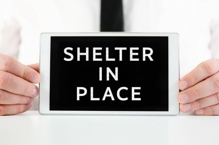 Businessman holding a smart tablet with sign Shelter in Place on screen, encouraging people to stay homeの写真素材