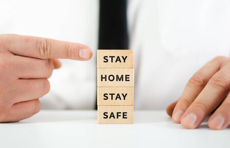 Hand of a businessman pointing at stack of wooden blocks with sign Stay Home Stay Safe, encouraging people to stay homeの写真素材