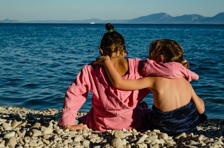 Sisters sitting by the sea  after swimming, hugging each otherの写真素材