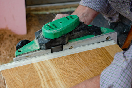 Worker planing the edge of massive oak stair with electrical plainer
