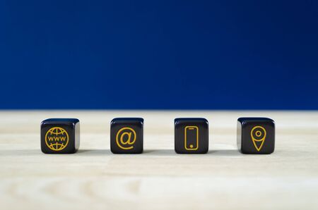 Wide view of customer service image with four black dices with gold contact information and location icons on them. Over blue background.の写真素材