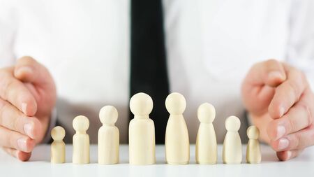 Male and female wooden figures representing workers with  hands of a businessman making protective gesture around it in a conceptual imageの写真素材