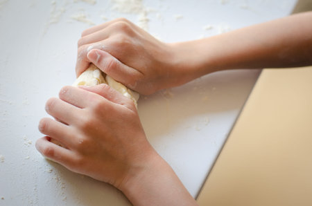 Hands of a kid girl kneading dough on a kitchen counter