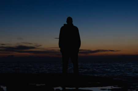 Silhouette of a man standing on the shore after sunset