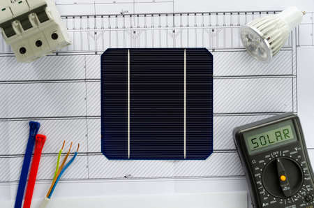 Planing the switch to solar power. Construction plan or blueprint and solar cells with mlultimeter, led bulb, breaker and cablesの写真素材