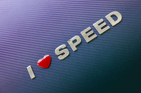 Love of speed, fast cars, motor racing. Letters with a red heart symbol on a green and violet carbon fiber background placed diagonally.の写真素材