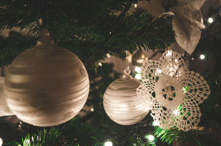 Close view of lace  ornament hanging on christmas tree with silver, white balls and christmas lightsの写真素材
