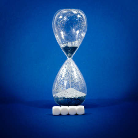 Four blank white blocks with copy space in front of  running hourglass  in a conceptual image. Side view, over blue background.の写真素材
