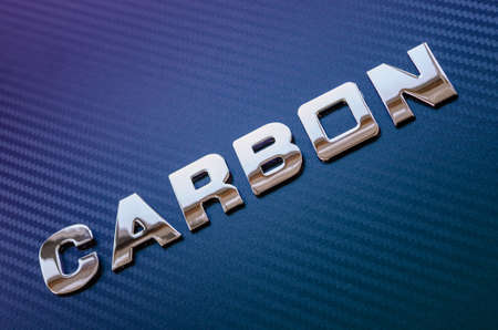 Concept of sport, speed, racing and lightweight.  Word carbon spelled diagonally in chrome letters on violet-blue carbon fiber background.の写真素材