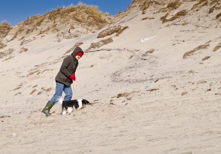 Woman walking small dog in dunes on a clear spring day with blue sky.の写真素材