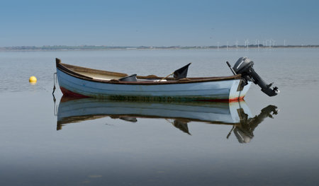 Small blue motorboat anchored up and reflecting in water.の写真素材