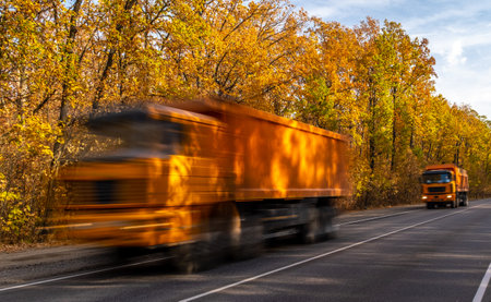the truck is orange in color with a high speed race around the track on the background of autumn trees with orange autumn foliageの写真素材
