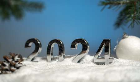 Background for New Year and Christmas cards, symbols of 2024 under the branches of a Christmas tree among gifts and snowの写真素材