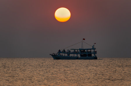 A sea pleasure boat with tourists on the background of the orange disc of the sun setting over the horizonの写真素材