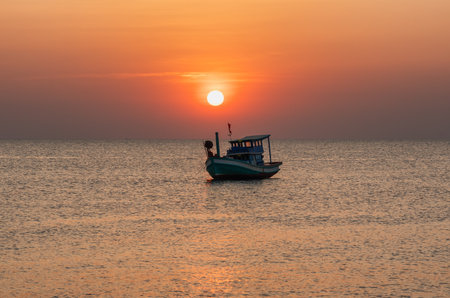 A scenic sunset at sea with a boat surrounded by calm waters and a fiery sky in the background. The setting sun adds a soft glow to the frameの写真素材