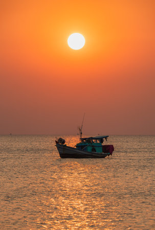 A scenic sunset at sea with a boat surrounded by calm waters and a fiery sky in the background. The setting sun adds a soft glow to the frameの写真素材