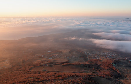 Aerial view of hills and small settlements surrounded by clouds at sunriseの写真素材