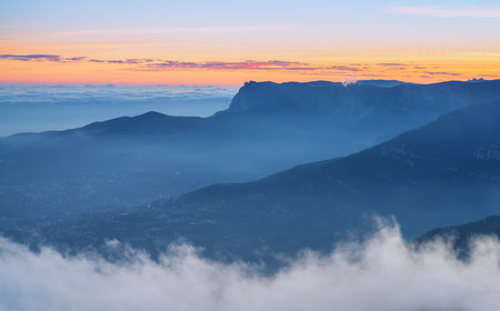 Majestic mountain silhouettes against the soft hues of sunrise and cloudsの写真素材