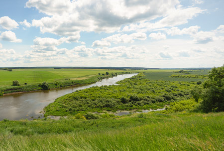 Summer landscape with a winding river and green fields under a cloudy skyの写真素材
