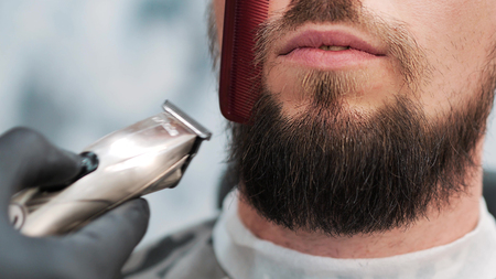 Barber is cutting the clients using red comb and electric shaverの写真素材