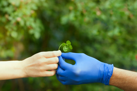 A man in a blue protective glove gives a clover leaf to a woman without gloves. A hand with blue...