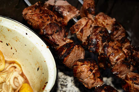 Closeup of some meat skewers being grilled in a barbecue.Shish kebab and pan with onions and lemon.の写真素材