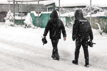 Two Ukrainian policemen walk a village street in snowy weather. Ukrainian police.の写真素材