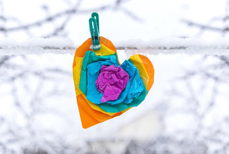 Multicolored paper heart on a clothespin. Heart from crumpled paper on a snowy background.