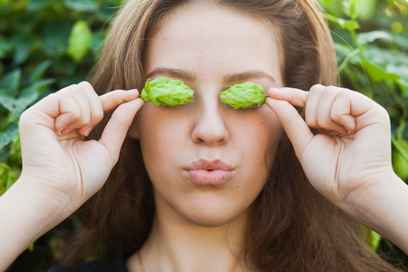 Closeup portrait of young woman holding hop, girl hiding her eyes with hopsの写真素材