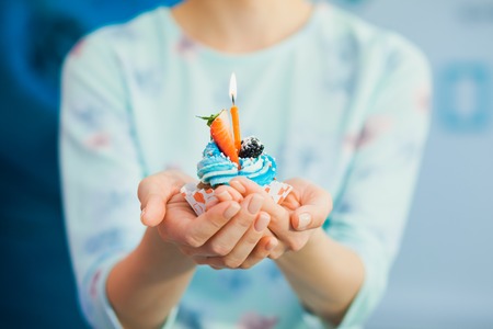 Female hands with birthday cupcake decorated with fruit. Making wish, holiday concept.の写真素材