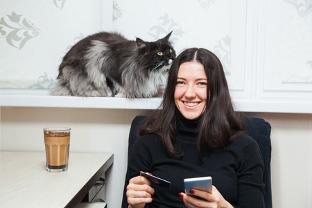 Young woman and cat buy things online with credit card and smart phone. Shopping conceptの写真素材