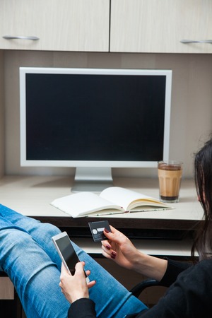 Young woman with credit card and smart phone sit by computer monitor. Onlina shopping conceptの写真素材
