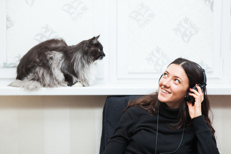 Beautiful girl listen to music and play with cat. Young woman in headphones at home.の写真素材
