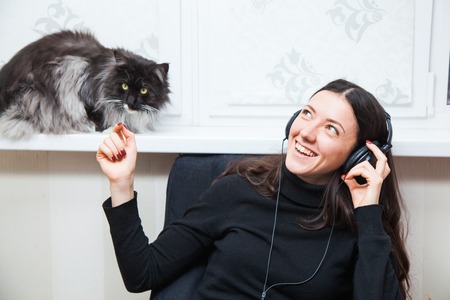 Beautiful girl listen to music and play with cat. Young woman in headphones at home.の写真素材
