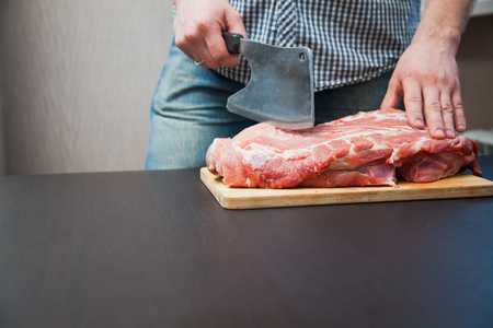 Piece of pork neck cutout on woodwn table. Man cutting meat with big knife. Male hands preparing marbled meatの写真素材