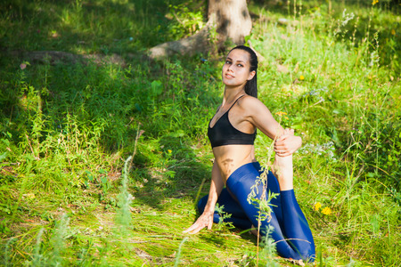 Beautiful fit woman fitness exercises outdoors. Go in for sports in nature forest and green grass. Stretching muscles. Yoga outsideの写真素材