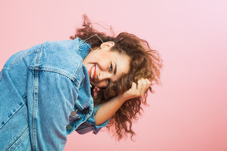 Beautiful young woman with curly hair in denim clothes. Trendy look, positive emitions, smile, copy spaceの写真素材