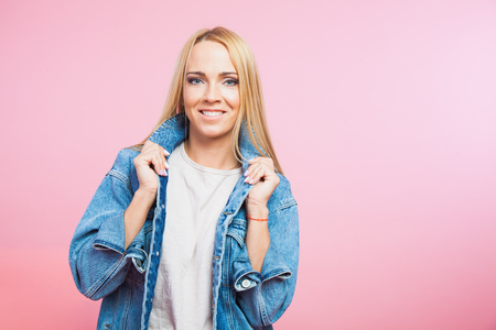 Portrait of beautiful blonde woman in jeans jacket smile and hold hair on pink backgroundの写真素材
