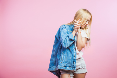 Portrait of beautiful blonde woman in jeans jacket smile and hold hair on pink backgroundの写真素材
