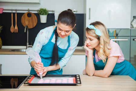 Two woman bakers dropping macaroons on mat. Girls on kitchen prepare french almond dessertの写真素材