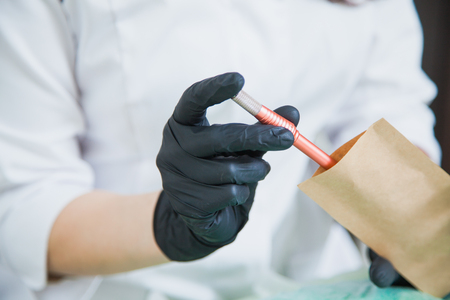 Female cosmetologist hand in black gloves put tattoo pen machine for microblading in craft package for sterilizationの写真素材