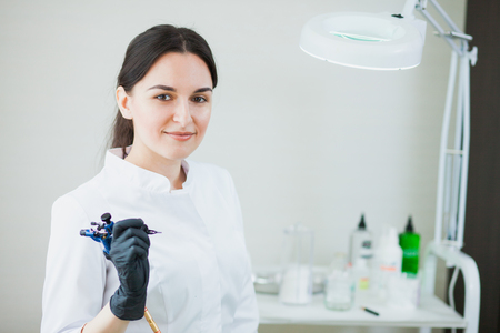 Female cosmetologist with tattoo machine for permanent makeup. Woman ready to make brow or lip correction by tattooingの写真素材