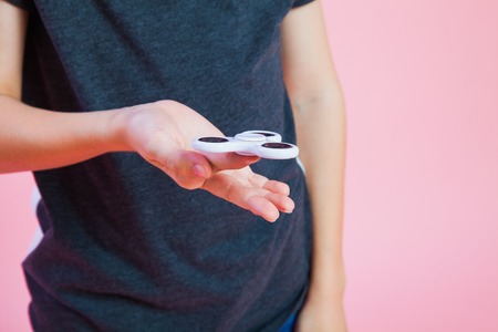Teenager with popular toy fidget spinner. Enxiety stress relief rotating plastic gadget. Studio shot pink background. Copy spaceの写真素材