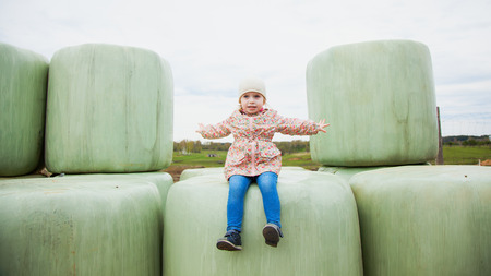 Pretty toddler girl sits on haylage, feel freedom. Rich harvest, horse feeding, countryside life. Copy spaceの写真素材
