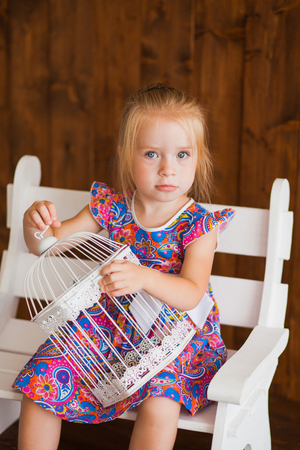 Portrait of a little girl in purple dress. Child hold white birdcageの写真素材