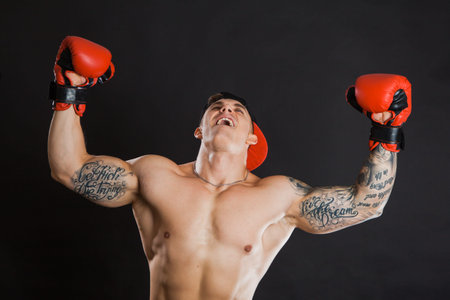 Muscular man in red boxing gloves raising hands. Win concept