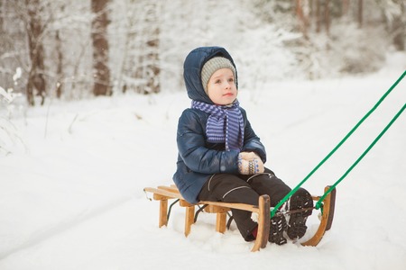 Little girl in winter jacket sit on sledge in snowy forest. Cold frosty dayの写真素材
